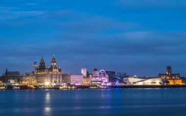 Dönen bir tekerlek ve diğer parlak araçlar Liverpool siluetinde Three Graces 'in önünde dikilirken parlıyor. Liverpool rıhtımı Mersey Nehri 'ne yansıyan yıllık festival alanına ev sahipliği yapıyor.