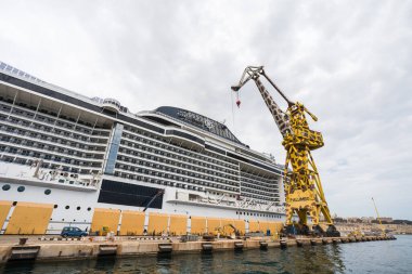 Nisan 2022 'de Valletta' da resmedilen Grand Harbour 'un kuru rıhtımındaki bir yolcu gemisinin yanında zürafa renginde bir vinç çalışıyor..