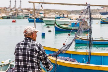 Nisan 2022 'de Malta' nın Marsaxlokk kentinde balık ağlarını teftiş eden bir balıkçı görülüyor..
