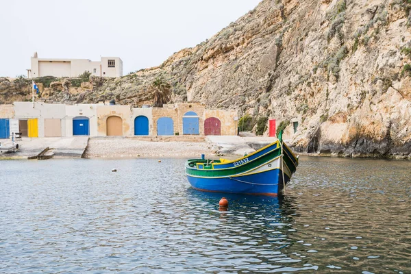 Nisan 2022 'de Malta' nın Gozo adasındaki Dwejra İç Denizi 'nde renkli tekne kulübelerinin önünde çekilmiş küçük bir Luzzu teknesi..