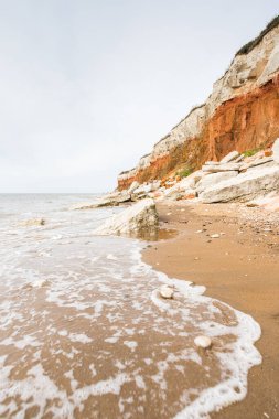 Kuzey Norfolk sahilindeki kırmızı ve beyaz kayalıkların altında Hunstanton sahilinde dalgalar kol geziyor..