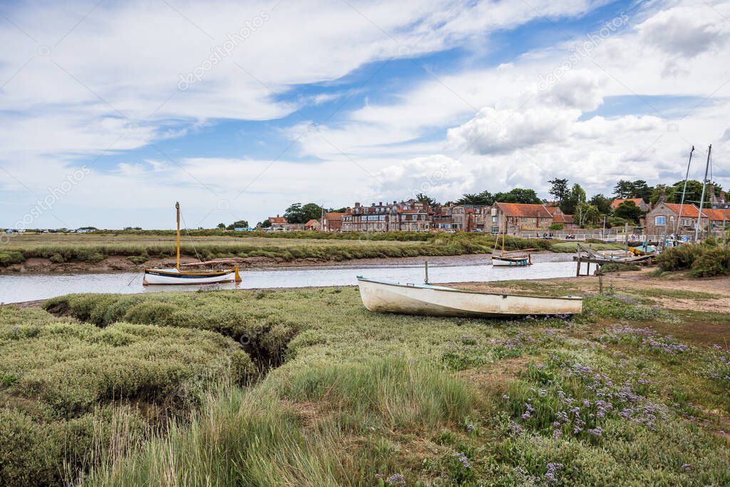 Blakeney village and boats seen between the green marsh plants and a blue sky on the North Norfolk coast in July 2022.