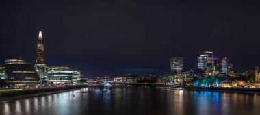 A multi image panorama of the London skyline and waterfront at night captured from Tower Bridge in August 2022.  Featured places of interest are the City Hall, The Shard, HMS Belfast, London Bridge, the Square Mile and the Tower of London.