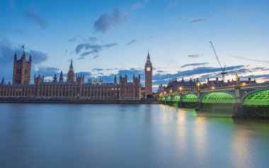 The underside of Westminster Bridge lights up in green after sunset in London during July 2022 as it leads towards the Houses of Parliament and Big Ben.