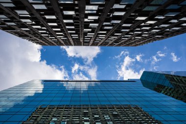 Looking towards a bright sky between two modern skyscrapers in London with clouds passing overhead.