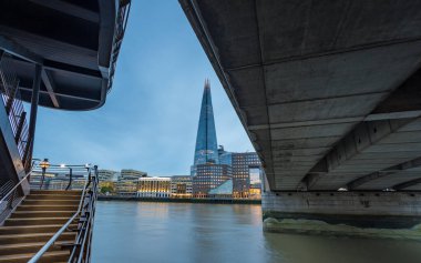 London Bridge and the spiral like staircase leading from the North Bank onto the bridge frame The Shard at twilight in August 2022.