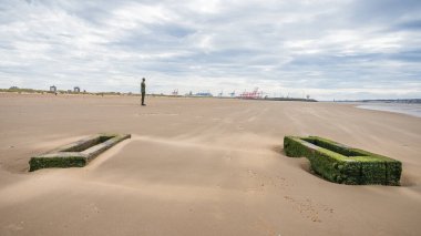 An Iron Man on a windy Crosby beach near Liverpool seen in August 2022 behind a pair of wooden pipe supports.