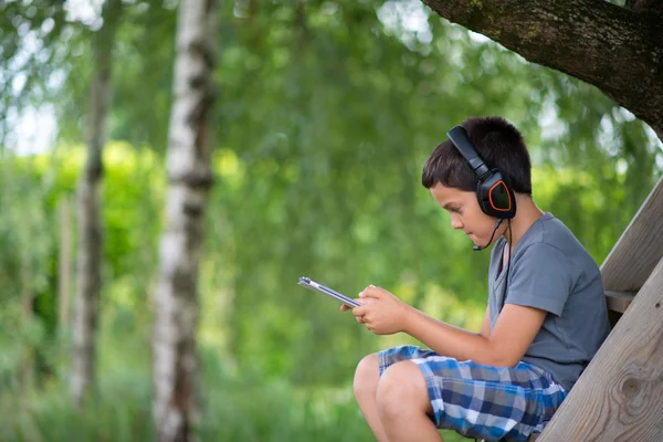 Niño jugando en el ordenador con auriculares al aire libre — Foto de Stock