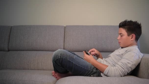 Adolescent garçon avec téléphone à la maison couché sur un canapé — Video