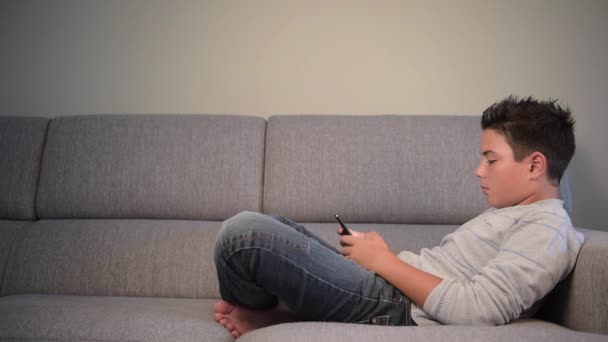 Genç çocuk evde telefon ile kanepede yatan — Stok video