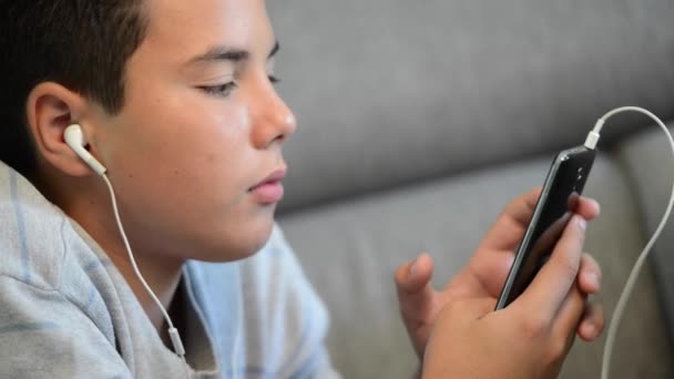 Jonge tiener liggen op een sofa luisteren naar muziek op zijn telefoon — Stockvideo