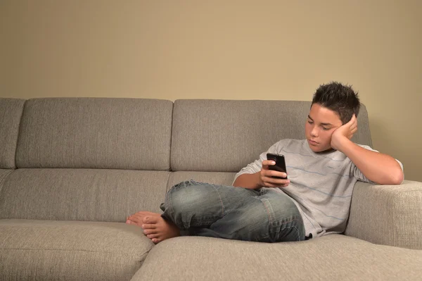 十几岁的男孩用手机在家里躺在沙发上 — 图库照片