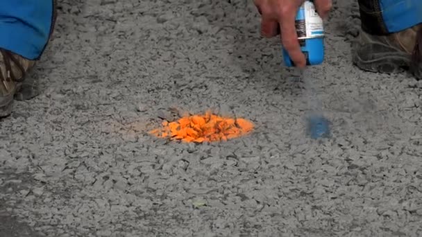 Trabajador marca una mancha en asfalto con pintura en aerosol florescente con un ajuste de plomada — Vídeos de Stock