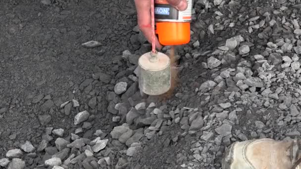 Trabajador marca una mancha en asfalto con pintura en aerosol florescente con un ajuste de plomada — Vídeos de Stock