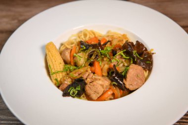 Tavada pişirilmiş domuz filetosu, siyah mantar ve Çin eriştesi, mısır koçanda, havuç, karamel sosu, soya, nuoc mama, zencefil, yüksek kaliteli fotoğraf.