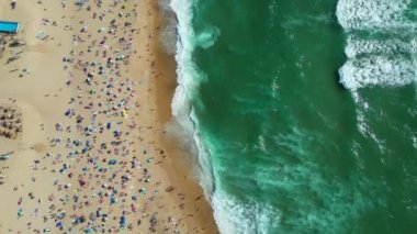 Top down aerial view of a beach in summer with holidaymakers on the beach and surfers on the waves, Basque Country. High quality 4k footage