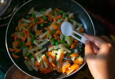 Kadın el, tavada sebzelere tuz ekliyor. Mutfakta sebze yapıyor. Seçici odak