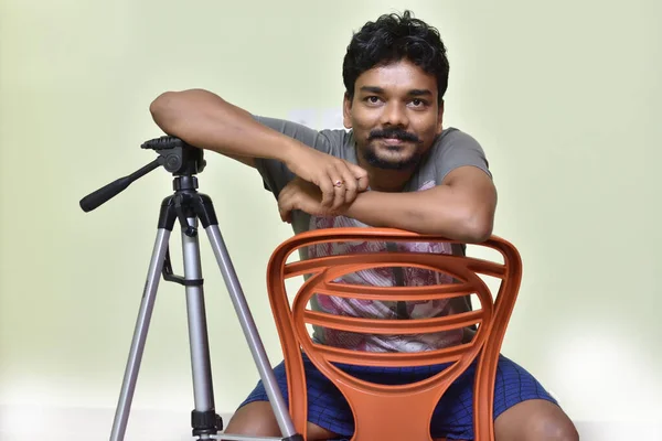 笑顔の肖像幸せなインドの男は半ズボンとTシャツで自宅で白に隔離された椅子に座っています — ストック写真