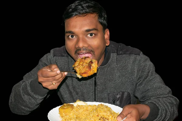 Indian man eating spicy homemade biryani chicken on black background