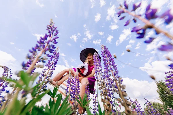 Gökyüzü ve lupinlerin arka planında şapkalı bir kız.