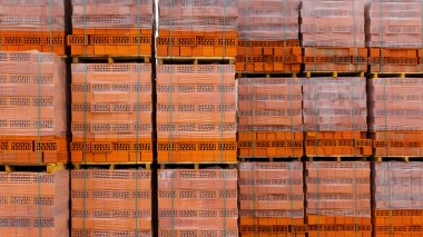 Kırmızı tuğlalar bir nalbur deposunda yerde saklanıyor. Dışarıdaki bir depoda paletlere tuğla örüyorlar..