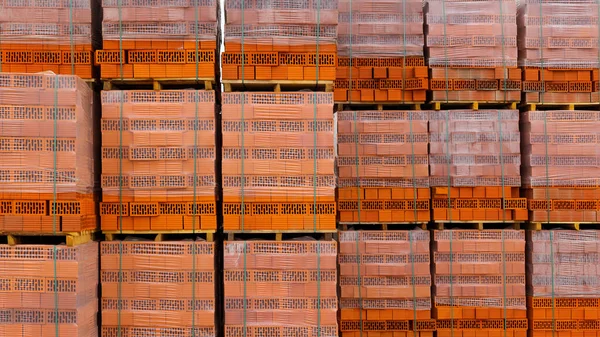 Kırmızı tuğlalar bir nalbur deposunda yerde saklanıyor. Dışarıdaki bir depoda paletlere tuğla örüyorlar..