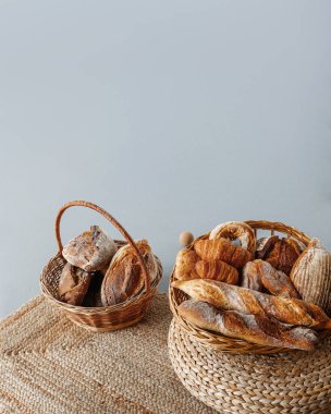 Taze hamur işleriyle dolu iki sepet: ekmek, ekmek, kruvasan, gri arka planda çörekler.