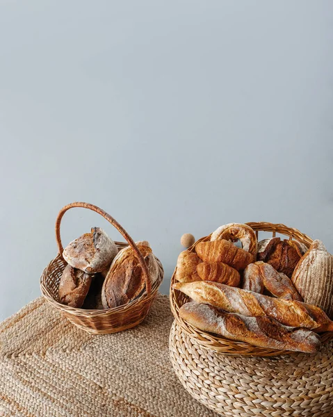 Taze hamur işleriyle dolu iki sepet: ekmek, ekmek, kruvasan, gri arka planda çörekler.
