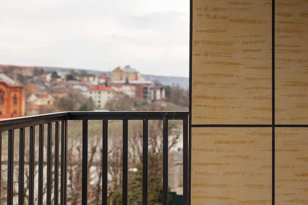 Çok katlı bir binanın geniş kıvrımlı balkonunda metal, siyah, desenli demir parmaklıklar var. Balkon konut kompleksinin, dağların ve bulutların evlerinin manzarasını sunuyor..