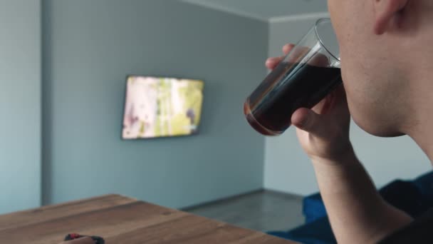 Ein Mann schaut fern und trinkt einen Drink, Seitenansicht, Nahaufnahme — Stockvideo