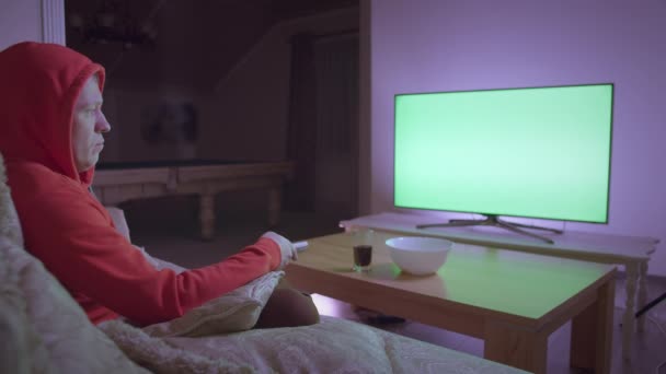 Mannen i huvan tittar på TV, sitter på soffan hemma på kvällen, kromakey — Stockvideo