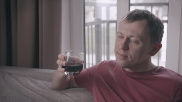 Üzgün adam elinde bir bardak içkiyle kanepede oturuyor. — Stok video