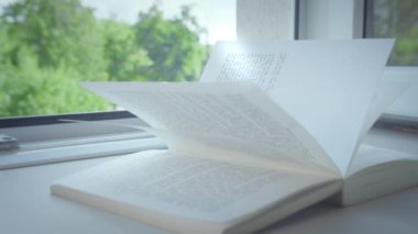 Açık kitap pencere kenarında yatıyor, güneş ışığı sayfalarda parlıyor.