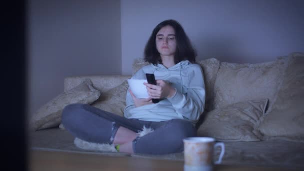 Вночі дівчина їсть фішки, дивиться телевізор, перемикає канали — стокове відео
