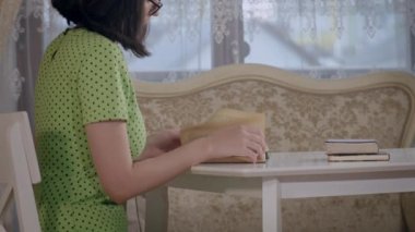 Masada otururken kitap okuyan bir kızın yan görüntüsü.