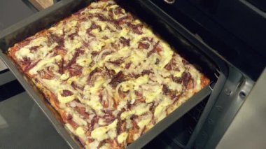 Adam fırına pizza kalıbı sokuyor, yakın plan.