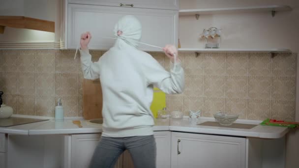 Chica morena bailando con una capucha en la cabeza, fondo de cocina, emociones positivas — Vídeo de stock