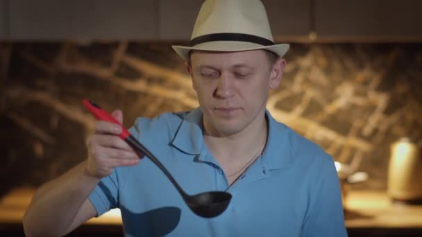 Hombre en un sombrero con un cucharón se para en frente de la cocina, degustación de alimentos de la cuchara, degustación de la comida — Vídeos de Stock