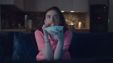 Esmer kız patates cipsi yiyor ve geceleri televizyon seyrediyor.