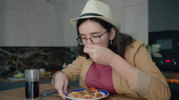 Une fille dans un chapeau avec des lunettes, manger et naviguer dans une application mobile — Video