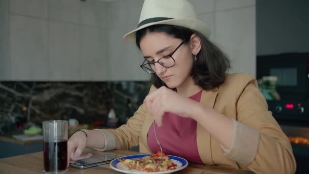 Hübsches Mädchen mit Hut und Brille, Essen und Surfen in einer mobilen App — Stockvideo
