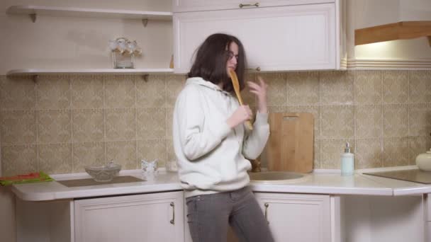 Chica morena bailando y cantando delante de la cocina con una espátula de madera — Vídeos de Stock