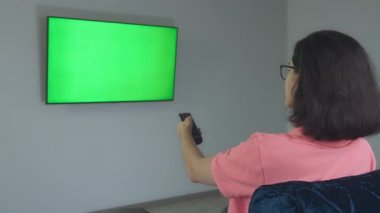 Duvarda asılı televizyon, kanepede oturan bir kız uzaktan kumandayla kanal değiştiriyor, kromakey.