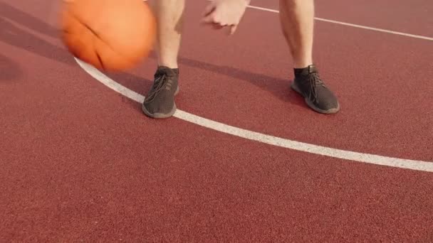 Kaki seorang pria berlatih keterampilan bola dengan menggulung bola basket antara kedua kakinya di lapangan terbuka di musim panas — Stok Video