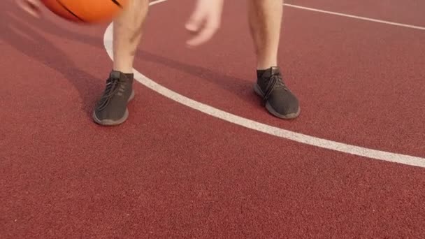 男子腿练习球技术，方法是在室外场地上双腿间滚动篮球，摄像机跟踪 — 图库视频影像