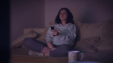 Esmer kız geceleri evde oturur ve kanepede otururken televizyon izler.