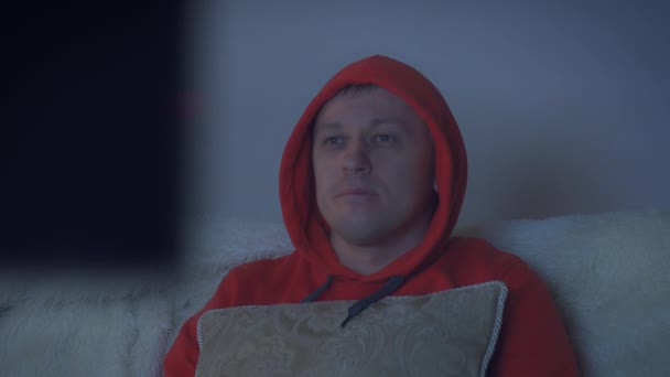 Un bărbat într-o capotă care se uită la televizor noaptea, urmărind o cameră — Videoclip de stoc