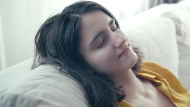 Расслабленная девушка сидит на диване с закрытыми глазами, закрывая глаза — стоковое видео