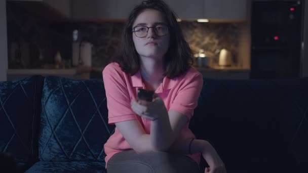 Lány szemüveg otthon este tévézni, miközben ül a kanapén, konyha háttér, elölnézet — Stock videók
