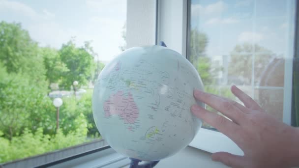 L'homme tourne le globe, qui se tient sur le rebord de la fenêtre par la fenêtre ouverte, choisit l'itinéraire pour voyager — Video